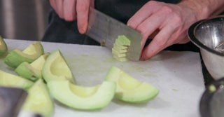 Close up view of an avocado that is being diced with a knife