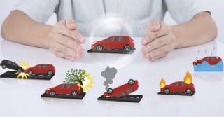 toy cars on a table depicting different auto claims scenario, including engine fire, rollover, hitting a tree.  One Toy car has a shield around it, symbolizing insurance coverage
