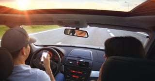 Behind view of a couple driving in a car.  The driver is checking their phone