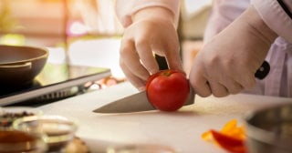 latex gloved hands slicing a tomato with a knife