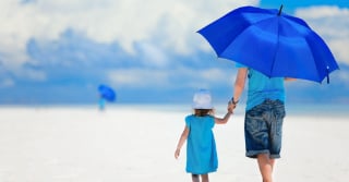 Man and Child walking on the beach with a blue umbrella 