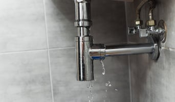 Damaged pipe with leaking water on grey background