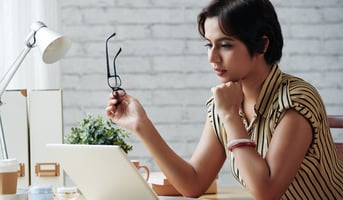 woman reading emails with her glasses in her hand looking pensive