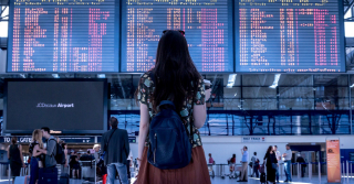 woman with backpack looking at the flight board in an airport terminal 