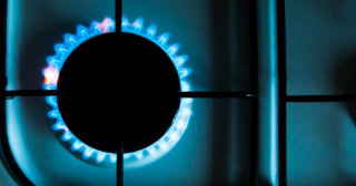 Close up of a stove burner. Burner is lit with blue flames