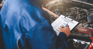 Man reviewing checklist while looking at the engine of a vehicle