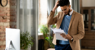 Confused man looks at paperwork while scratching his head