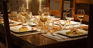 Dinner table that is set with placemats, napkins, plates, wine glasses, and cutlery - as if for a fancy dinner party