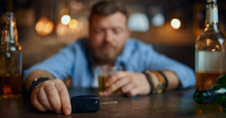 Man at a bar holding a shot of alcohol in one hand and his car keys in the other