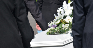 White casket with flowers being carried by men in suits