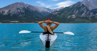 woman relaxing in kayak in a lake looking at mountains in distance