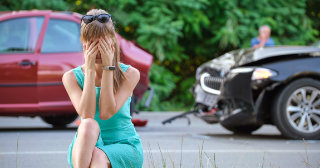 Distressed woman covering her face.  There is the aftermath of a car accident in the background