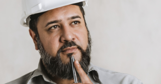 Bearded man in hard hat is thinking, has his finger on his chin