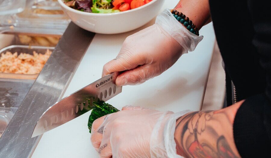 Person making salad, while cutting cucumber at a busy deli