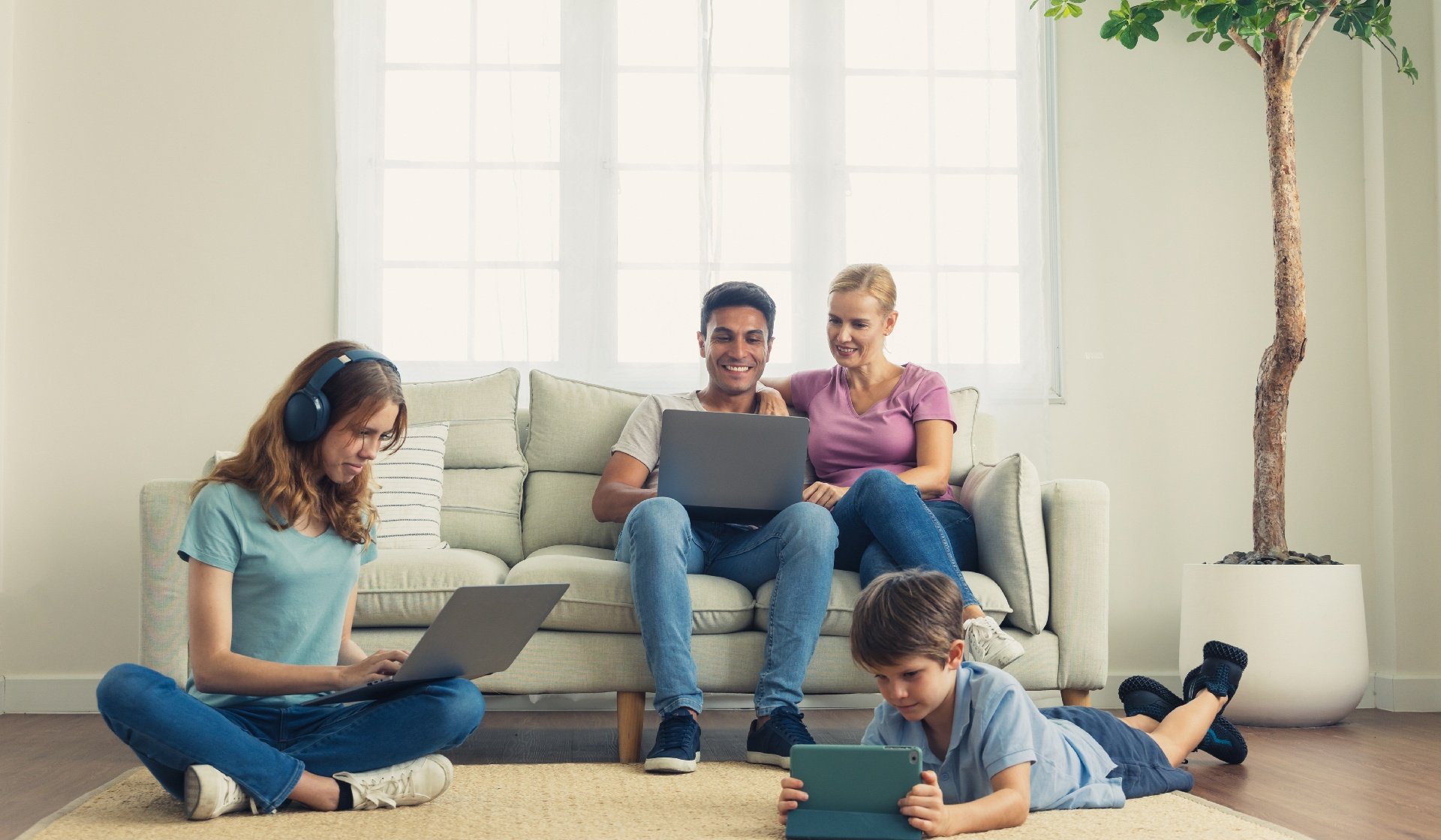 A parent and Children using a laptop, smartphone in the living room.