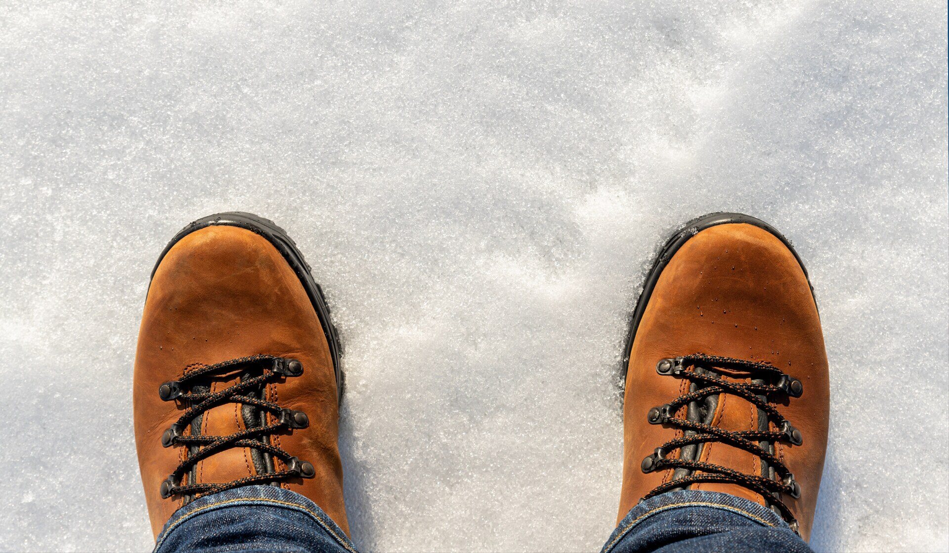 Closeup top above view of male legs in jeans and brown leather warm boots isolated on white icy snow