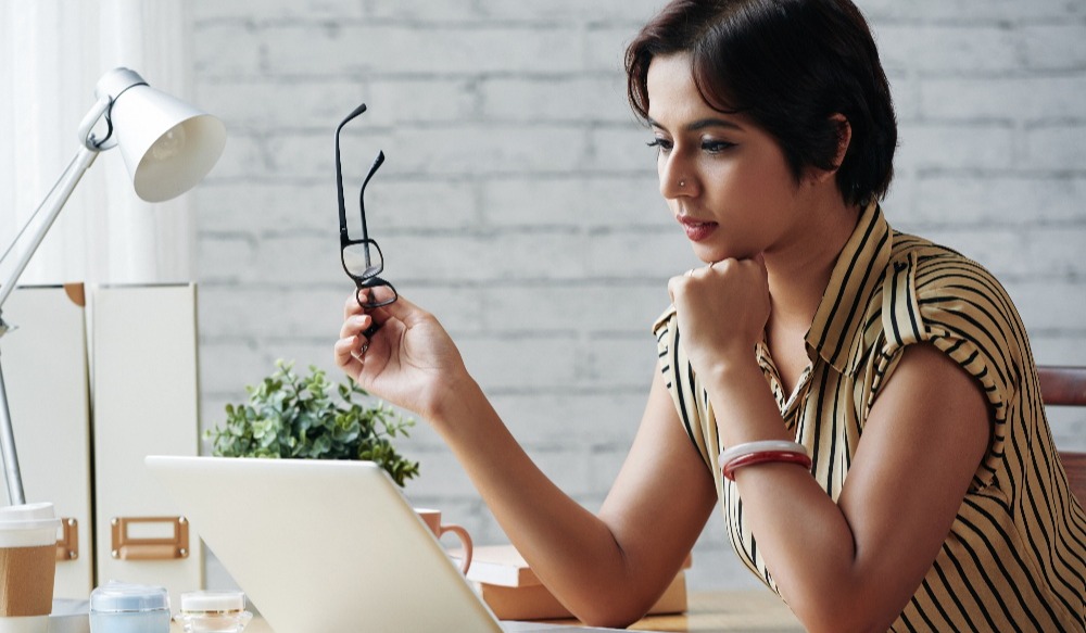 woman reading emails with her glasses in her hand looking pensive