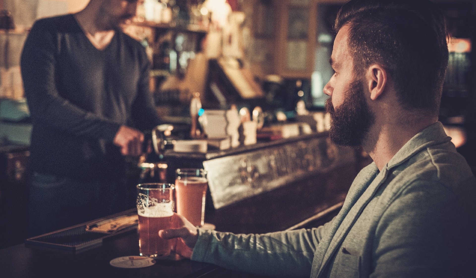 man sitting alone at bar counter with a pint of multiple beers