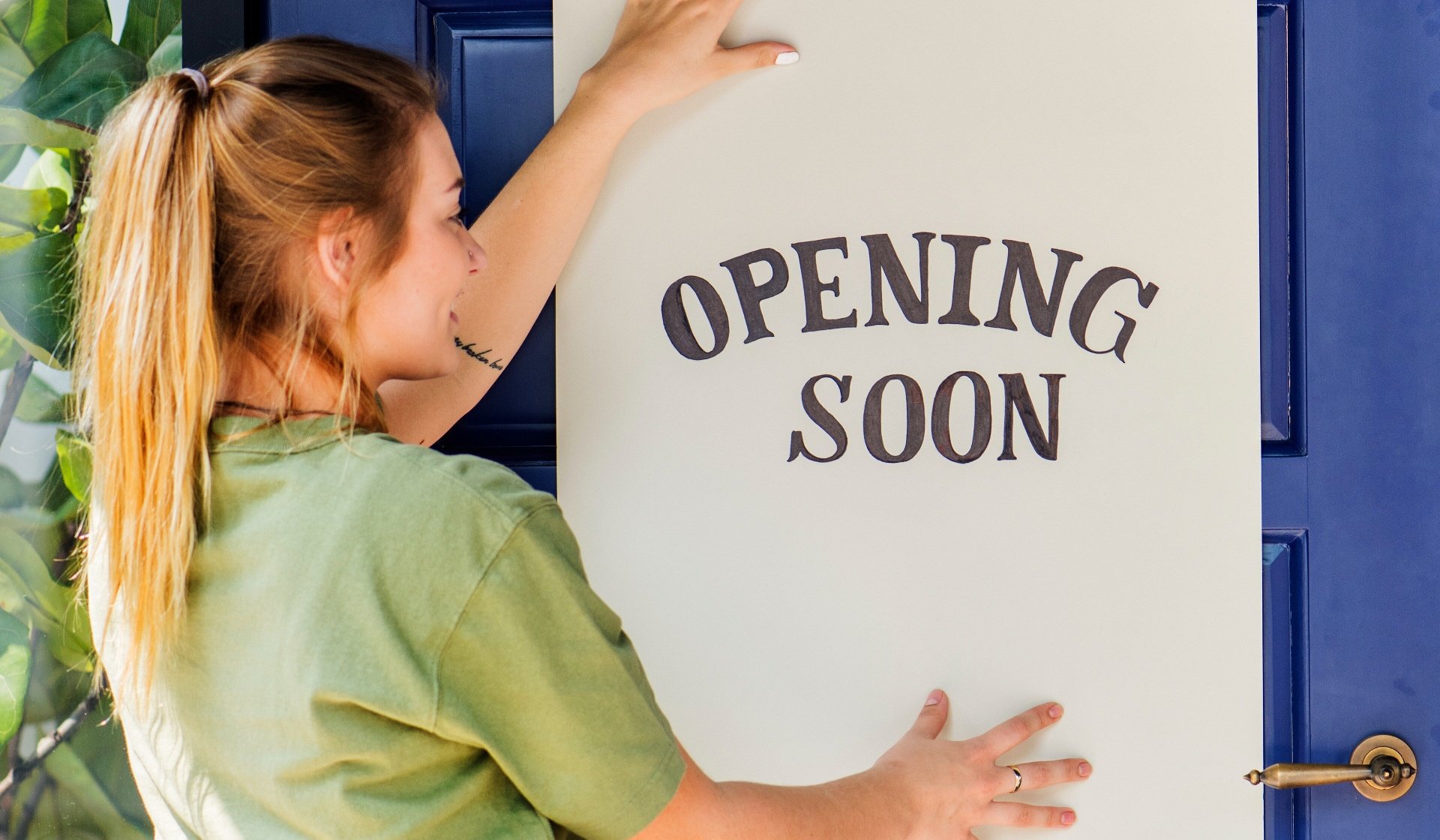 Woman putting on store opening soon sign